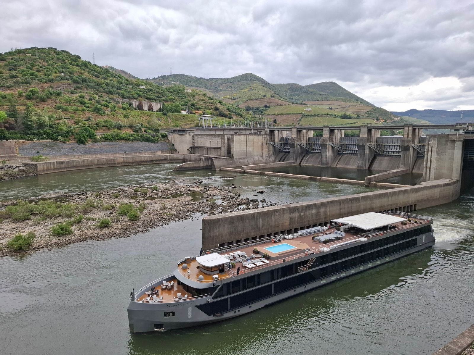 River cruise ship with a long sun deck sailing past a dam on the Douro in Portugal